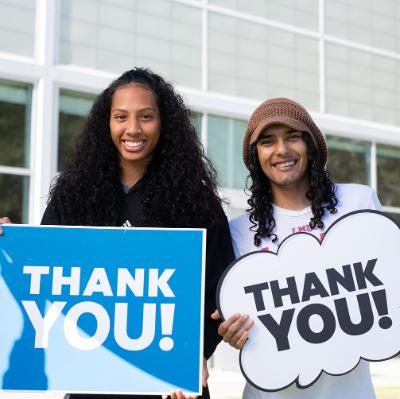 Two students stand outside holding thank you signs after the campus-wide Day of Giving campaign.