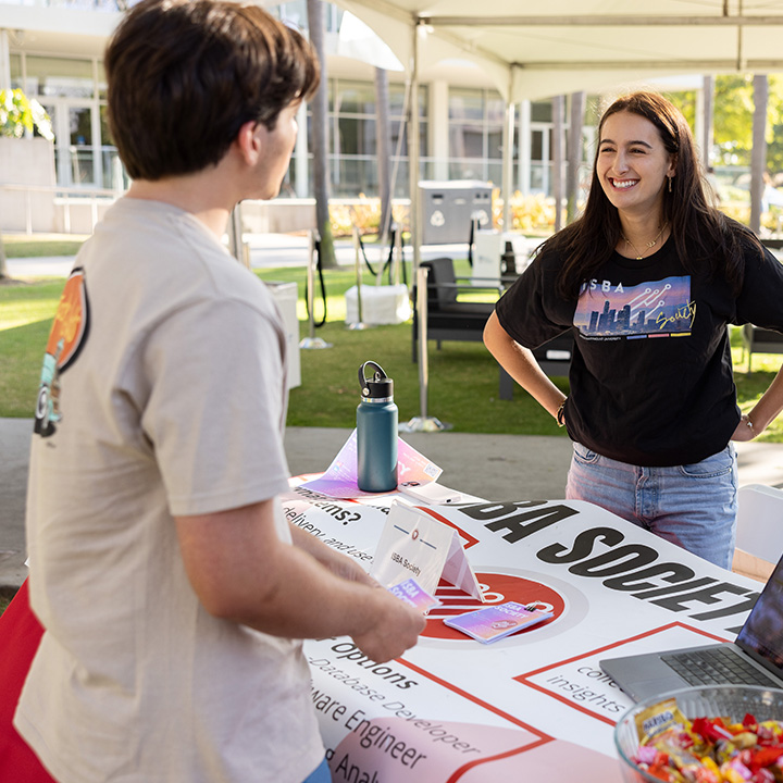 Two students converse at a campus involvement fair booth under a white canopy tent