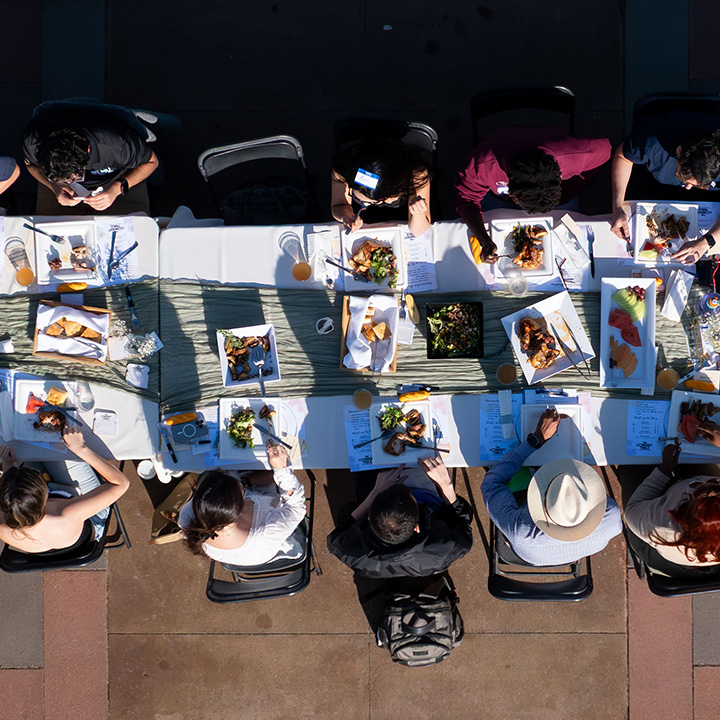 Overhead view of a long outdoor dining table where attendees are seated and sharing a meal