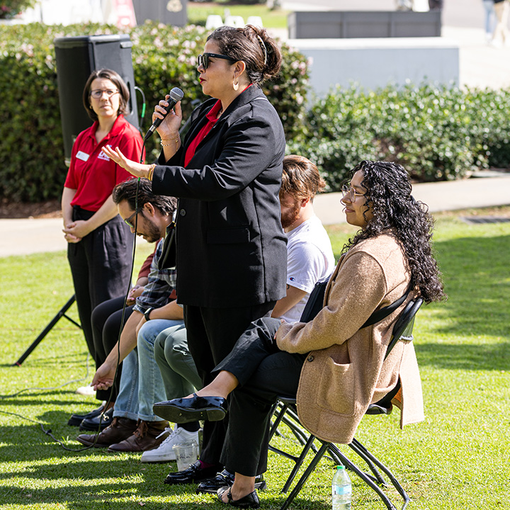 Staff members sit outside on chairs presenting using a mic.