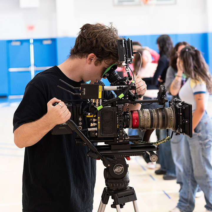 A student is looking into a black camera inside a gym.