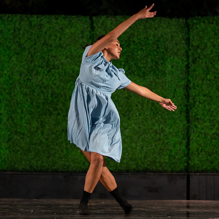 A single female dancer in a blue dress poses on the Drollinger Family Stage.