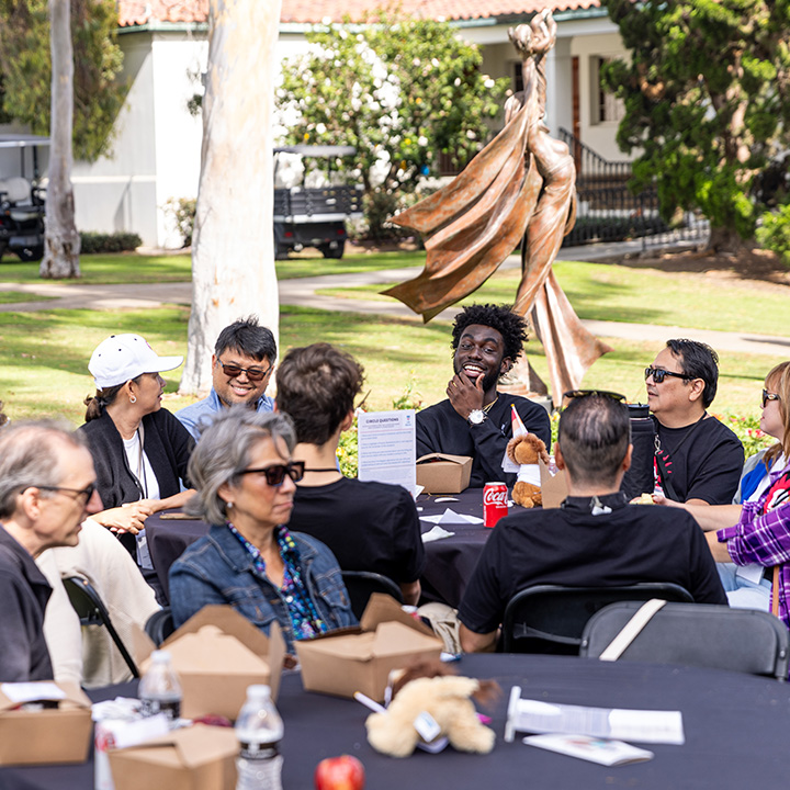 Parents and students gather outside at tables for a Family Weekend luncheon.