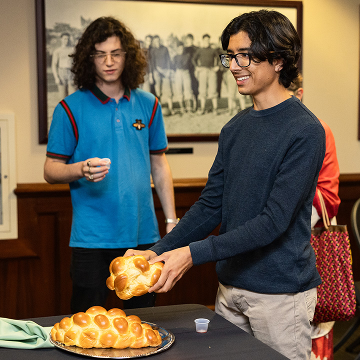 Two male students stand inside The Hill breaking bread for Shabbat.