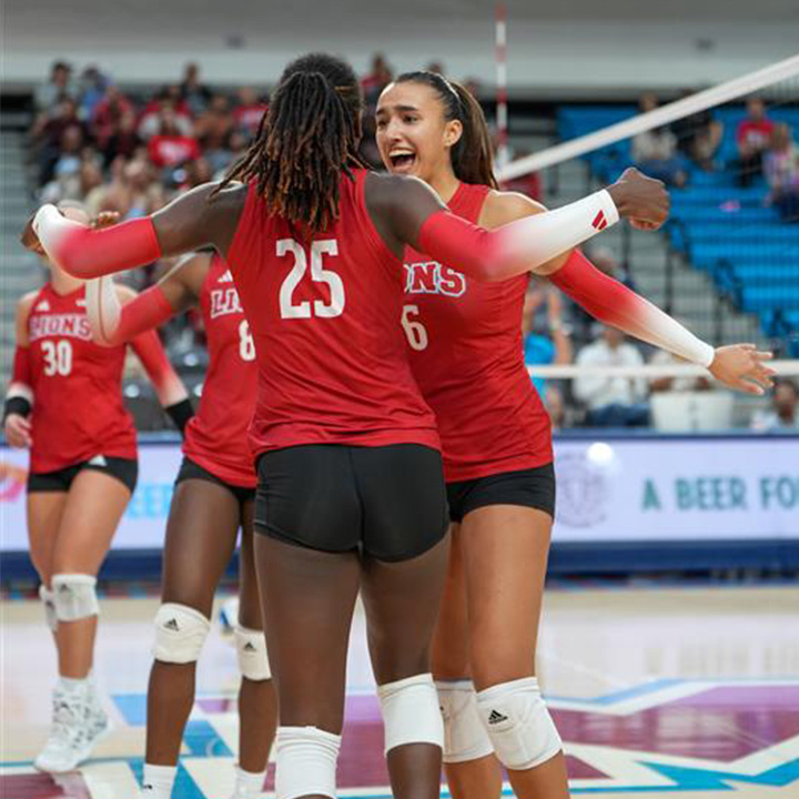 Two female students cheer and jump with red volleyball uniforms on.