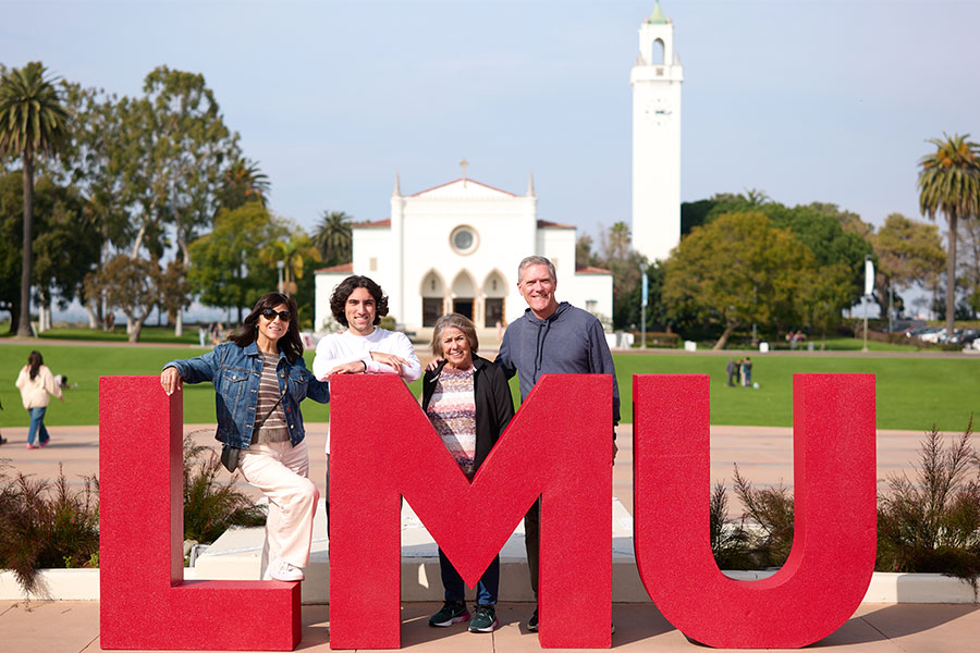 A Lion family poses with LMU letters on Regent's Terrace with Sacred Heart Chapel in the background.