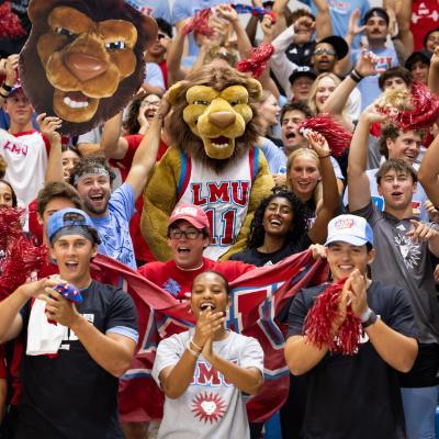 Students cheer in the stands at a basketball game with LMU's mascot Iggy the Lion.