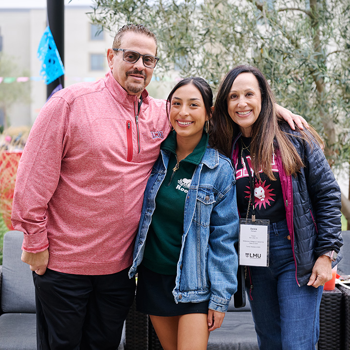 The person in the center wears a green polo shirt and a denim jacket, while the people on either side wear casual jackets and event name badges