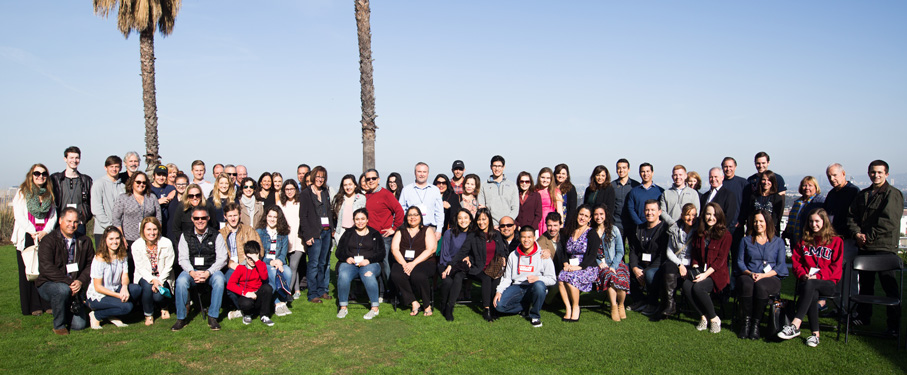 Large group of parents standing together on the bluff with palm tree trunks in the background